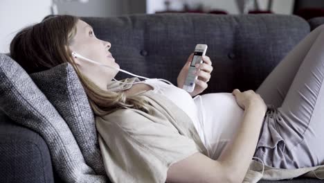 Smiling-pregnant-woman-having-video-call-while-lying-on-sofa